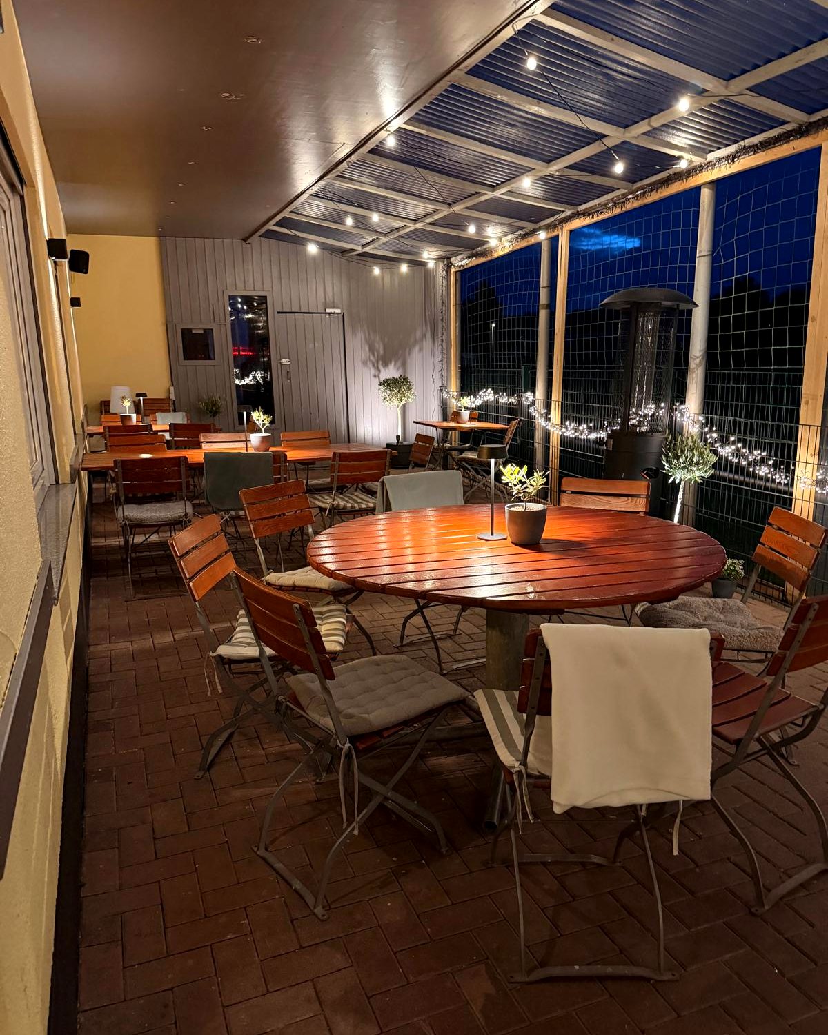 Überdachte Terrasse des Restaurants Bärenhöhle Grolsheim mit Lichterketten und Heizpilz am Abend